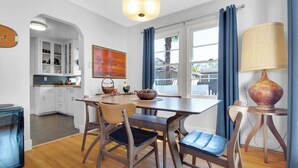 Una cocina moderna con armarios blancos, una mesa de comedor con sillas, una lámpara colgante y una ventana con cortinas.