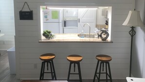 A kitchen with a window view, white cabinets, a refrigerator, a stove, and a sink. There are three wooden stools in front of the window.