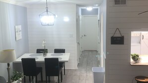 A modern living room with a sofa, a dining table with chairs, a lamp, and a hanging light fixture.