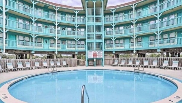 A large pool with a central diving board, surrounded by a multi-level building with balconies.