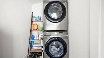 A laundry room with two stacked front-loading washing machines and a shelf with various cleaning products.