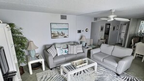 Ein Wohnzimmer mit grauem Sofa, weißem Sessel, Couchtisch und Deckenventilator.