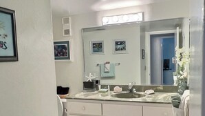 Ein Badezimmer mit großem Spiegel, Waschbecken und einem Waschtisch mit Schränken. An der Wand hängen gerahmte Bilder und es gibt einen Handtuchhalter.