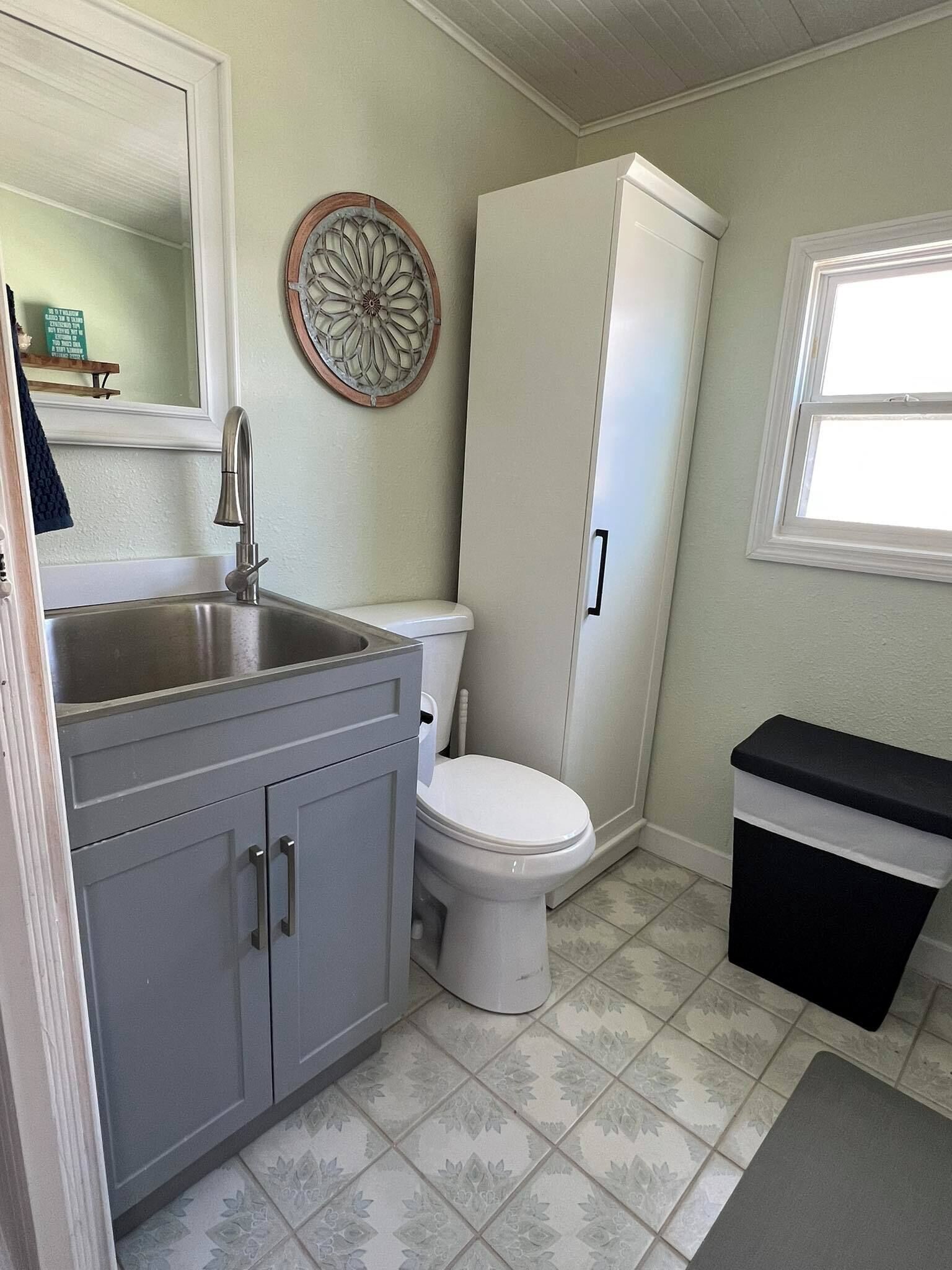 Une salle de bain avec des toilettes blanches, un lavabo avec un miroir et un meuble de rangement.
