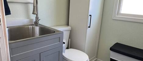 Une salle de bain avec des toilettes blanches, un lavabo avec un miroir et un meuble de rangement.