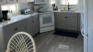 A compact kitchen with white cabinets, a microwave, stove, and a refrigerator. There's a wooden sign above the sink that reads "Life is Beautiful." - Newly Renovated 1 Bed/1.5 Bath Mobile Home Near Ft. Myers Beach, Florida (Fort Myers)