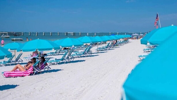A beach with rows of blue umbrellas and lounge chairs, a pier in the background, and a clear blue sky. - Newly Renovated 1 Bed/1.5 Bath Mobile Home Near Ft. Myers Beach, Florida (Fort Myers)