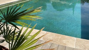 Piscina límpida com um edifício de pedra ao fundo, rodeada por vegetação e céu claro.