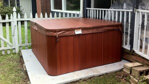 Un jacuzzi frente a una casa con valla blanca y una ventana.