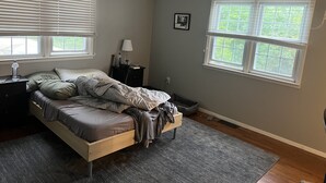 Un dormitorio con cama, mesita de noche, lámpara y dos ventanas.