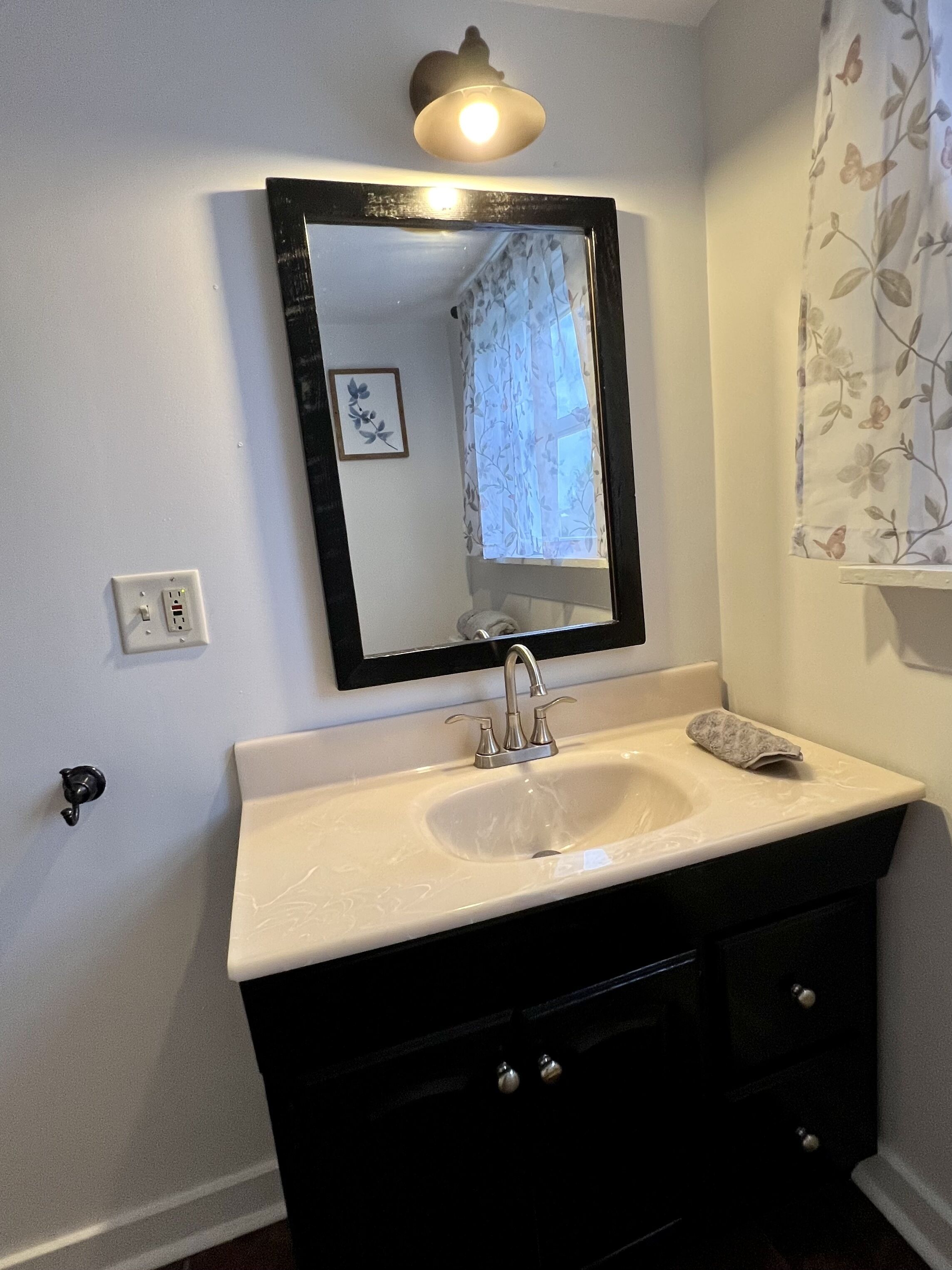 A bathroom with a white sink, black vanity, and a mirror above it.