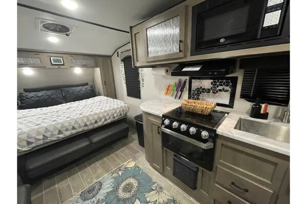 Compact RV with a kitchenette, small bed, and decorative rug.
