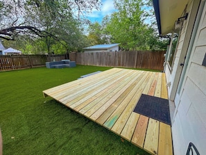 A backyard with a wooden deck, artificial grass, and a wooden fence. - Luxe Family Home | Sleeps 7 | South Austin! (Austin)
