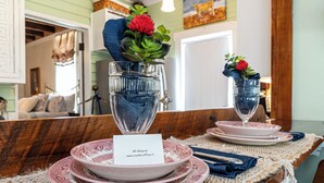 A dining table set with pink plates, a glass vase with a red flower, and a card with a name. - Charming 1-bedroom Pearl Cottage with WiFi in the historic Casey Jones Village (Jackson)