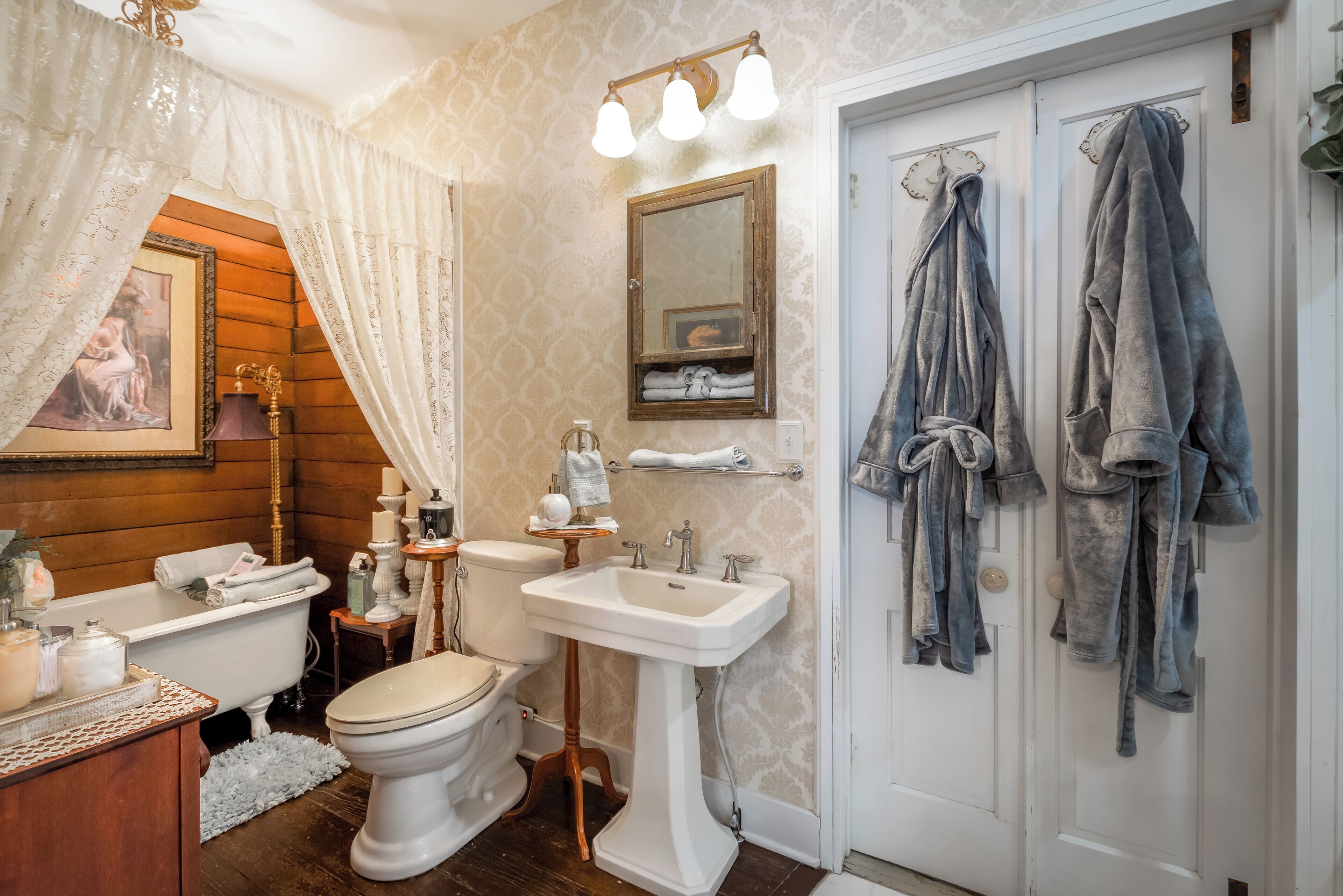Un bagno con vasca, water, lavandino e uno specchio. Asciugamani appesi al muro e una porta con porta-asciugamani.