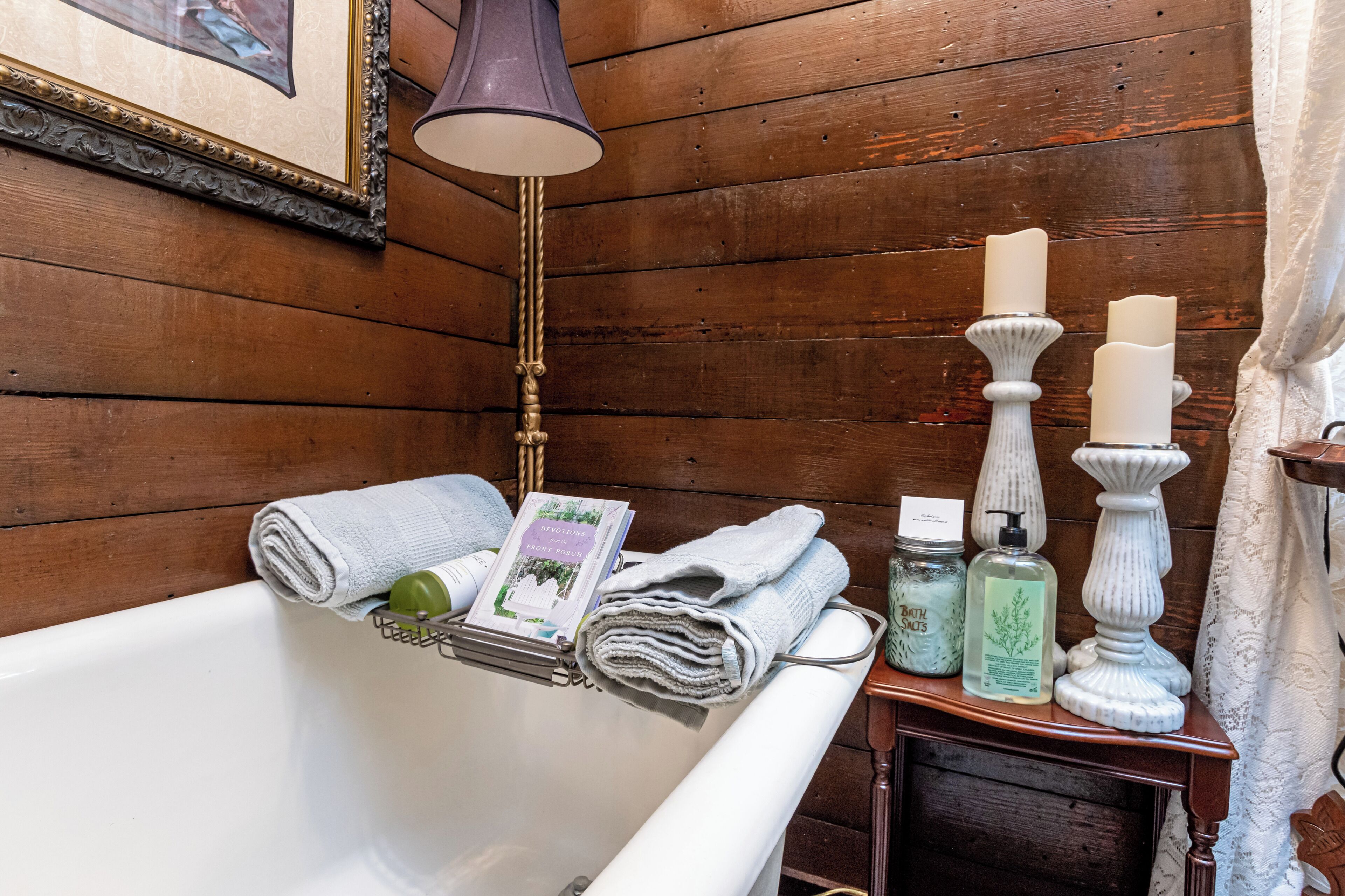 Ein Badezimmer aus Holz mit einer Badewanne, einem Handtuchhalter mit gefalteten Handtüchern, einem Buch, einer Flasche und einem Kerzenständer.
