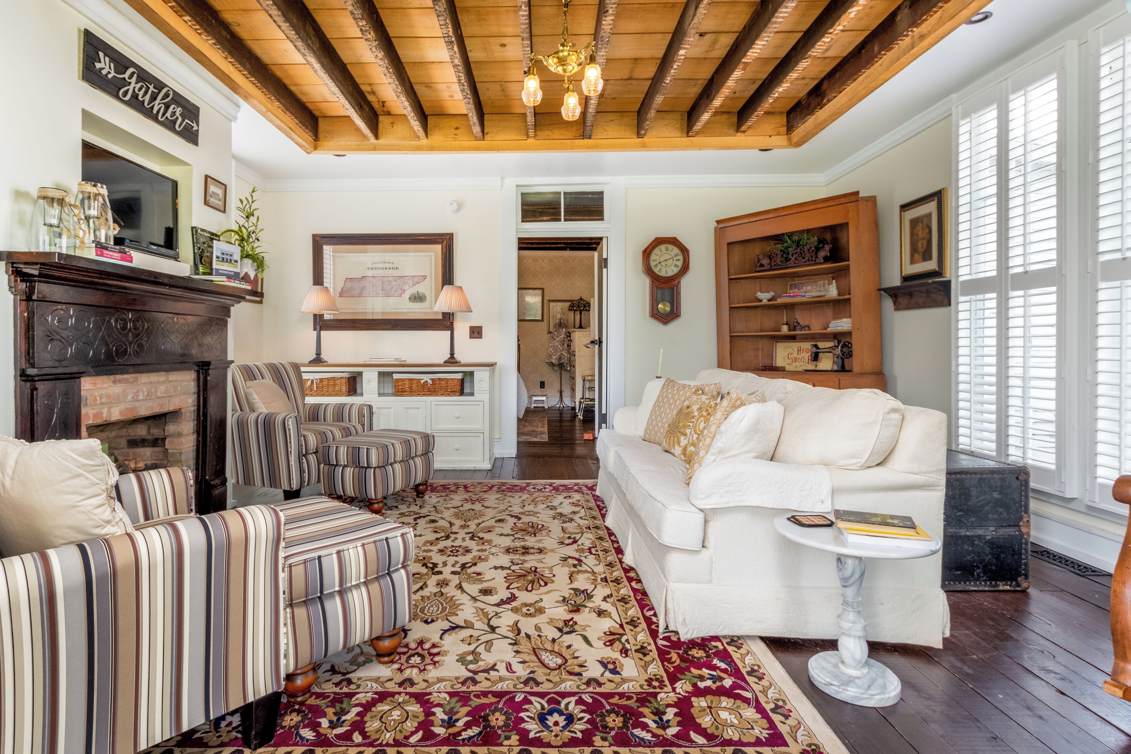 A cozy living room with striped sofas, a white sofa, a fireplace, and a wooden ceiling.