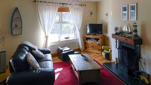 A living room with a sofa, a television, a fireplace, and a window with curtains. - Charming cottage in a traditional Irish fishing village. (Greencastle)