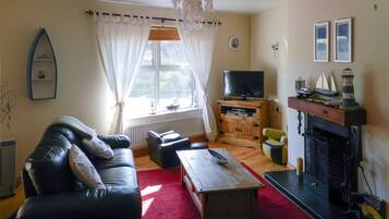 A living room with a sofa, a television, a fireplace, and a window with curtains.