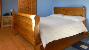 A wooden bed with white bedding in a room with blue walls and a wooden wardrobe. - Charming cottage in a traditional Irish fishing village. (Greencastle)