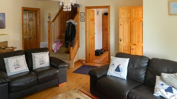 A living room with two black leather sofas, wooden flooring, a wooden staircase, and a chandelier. - Charming cottage in a traditional Irish fishing village. (Greencastle)