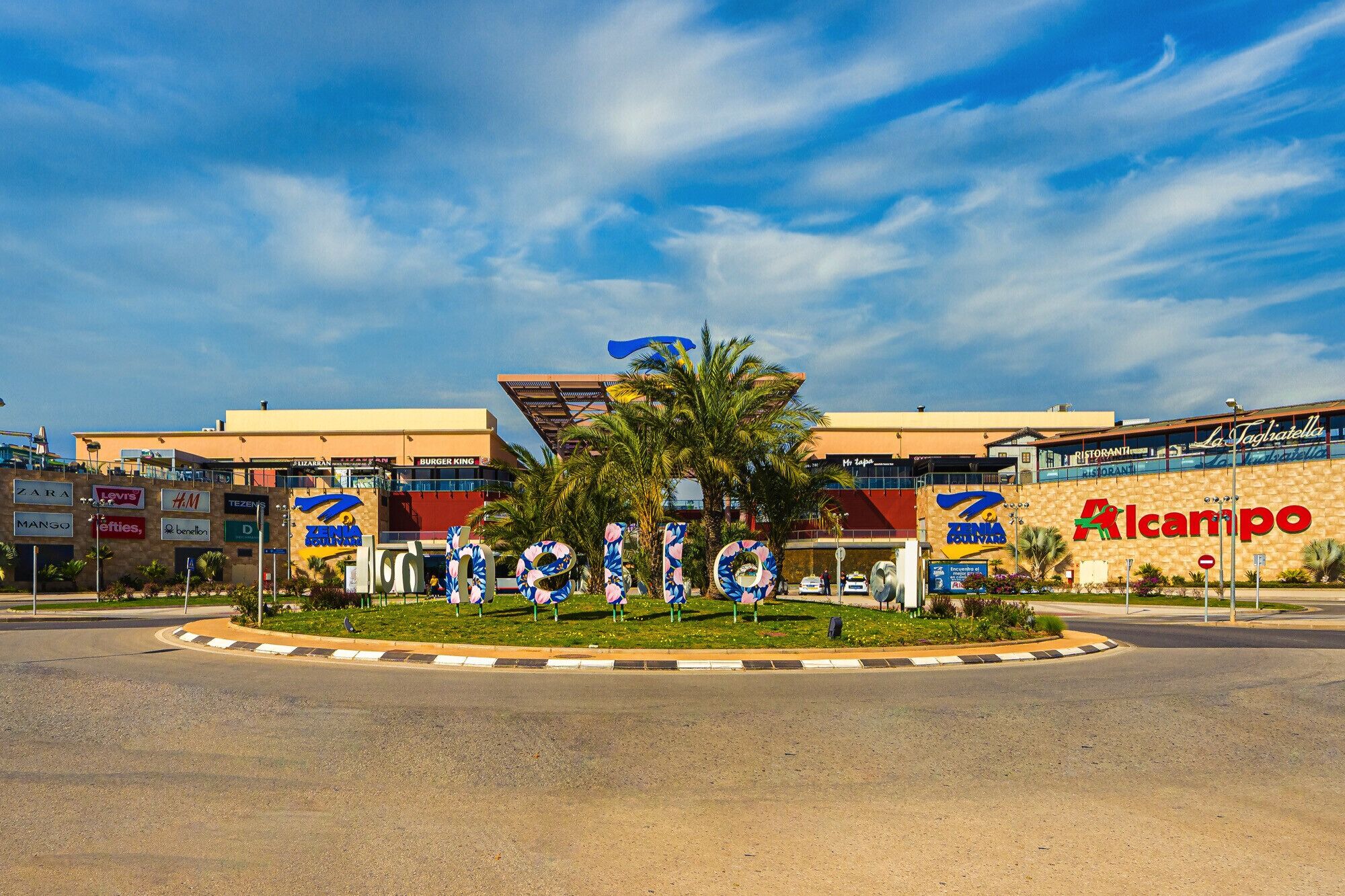 A commercial building with multiple storefronts, including a prominent 'Alcampo' sign.