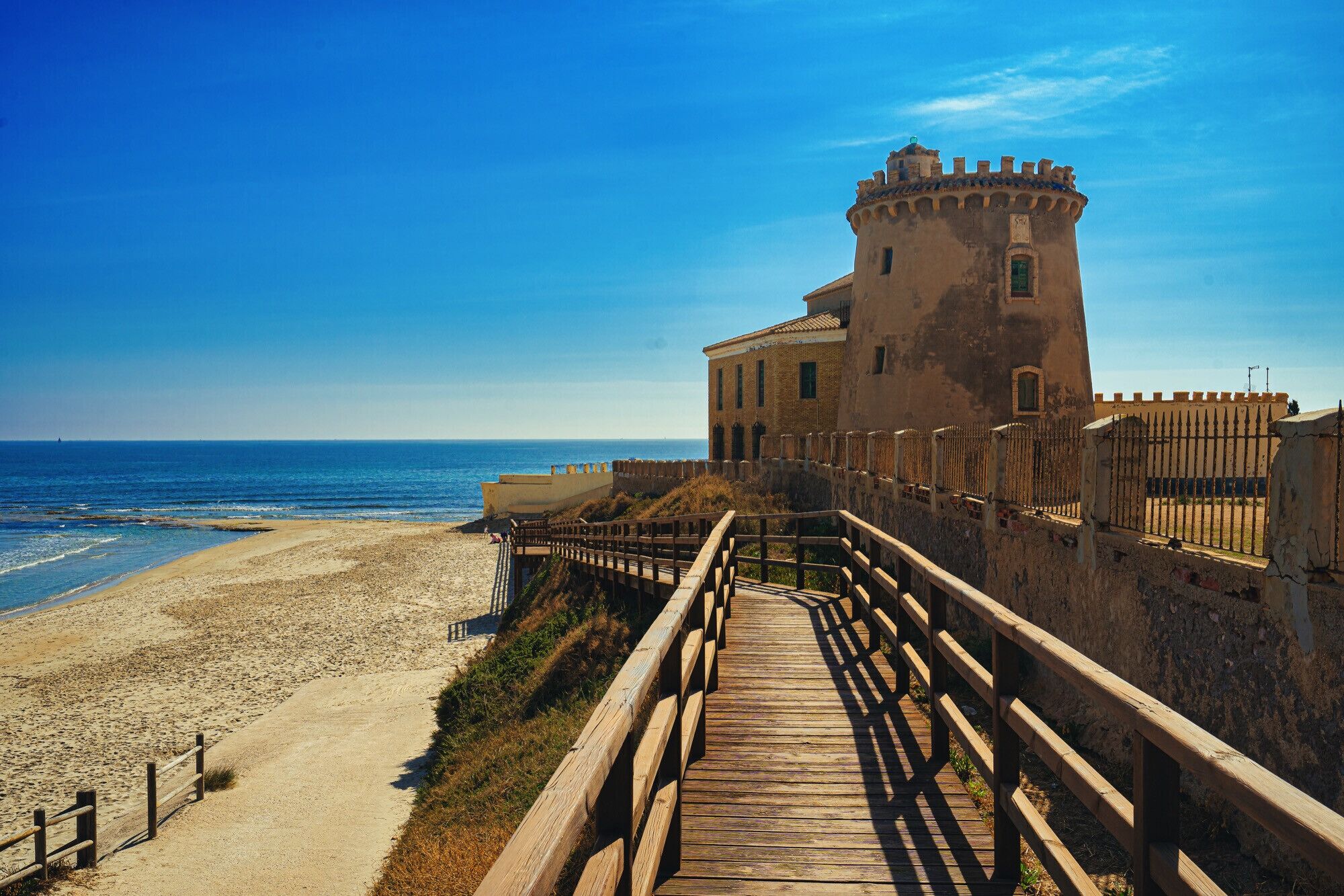 A coastal building with a wooden walkway leading to the beach.