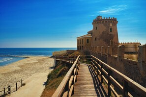 A coastal building with a wooden walkway leading to the beach. - Apartamento Las Violetas (Villamartin) (Orihuela Costa)