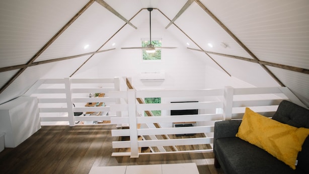 A spacious attic room with a sloped ceiling, white railings, a gray sofa with a yellow pillow, and a wooden floor.