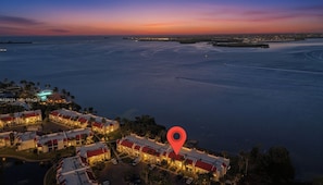 An aerial view of a coastal hotel with multiple buildings, a marina, and a sunset over the water.