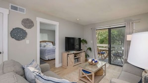 Een moderne woonkamer met een bank, een televisie, een salontafel en een balkon met tuinmeubilair.