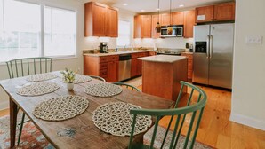 A modern kitchen with wooden cabinets, a stainless steel refrigerator, and a dining area with a wooden table and chairs. - 2BD-3BA-3BEDS in the PERFECT location in Ocean Springs! Britt's Creek Condo (Ocean Springs)