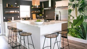A modern kitchen with a large island, bar stools, a hanging light fixture, and a refrigerator. - True Tropical Escape at The Coconut House (Fort Pierce)