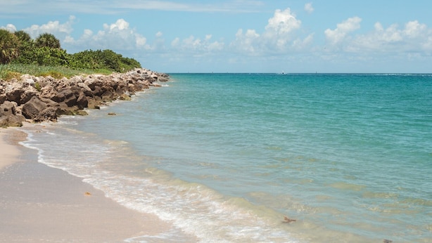 A beach with clear turquoise water, sandy shore, and rocky outcrops. - True Tropical Escape at The Coconut House (Fort Pierce)