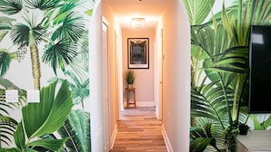A hallway with a tropical mural, a framed picture, and a potted plant. - True Tropical Escape at The Coconut House (Fort Pierce)