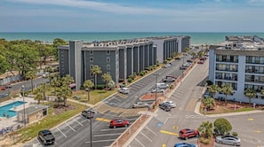 A multi-story hotel with a parking lot, a swimming pool, and a view of the ocean.