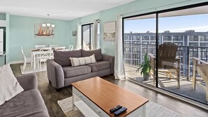 A modern living room with a grey sofa, a wooden coffee table, and a balcony with a view of the city. - NEW! Ocean-Front Resort, Steps From Beach, 6 pools and Lazy River (Myrtle Beach)