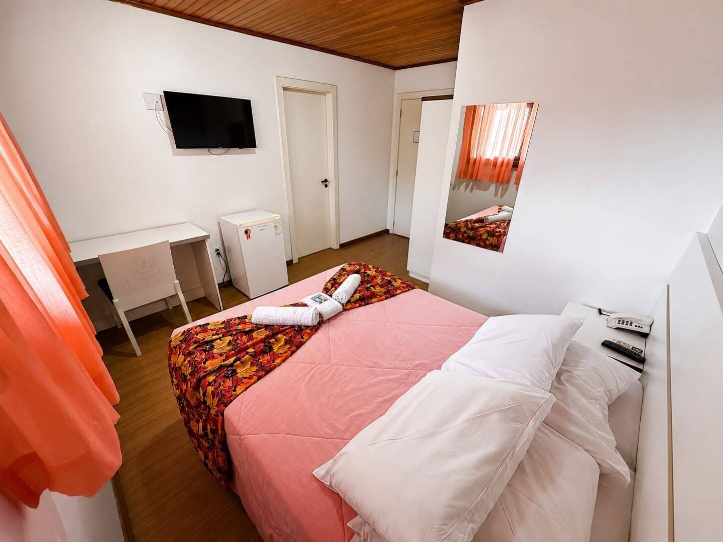 A hotel room with a bed, a desk, a TV, a mirror, and a phone.