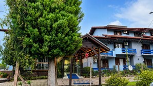 A building with a blue facade, a covered outdoor seating area, and a tree in the foreground. - Hotel Alpenhof (Gramado)