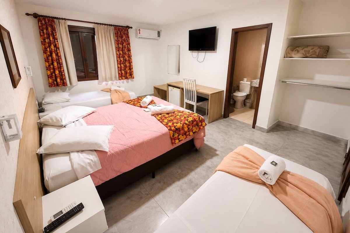 A hotel room with two beds, a desk, a TV, and a bathroom.