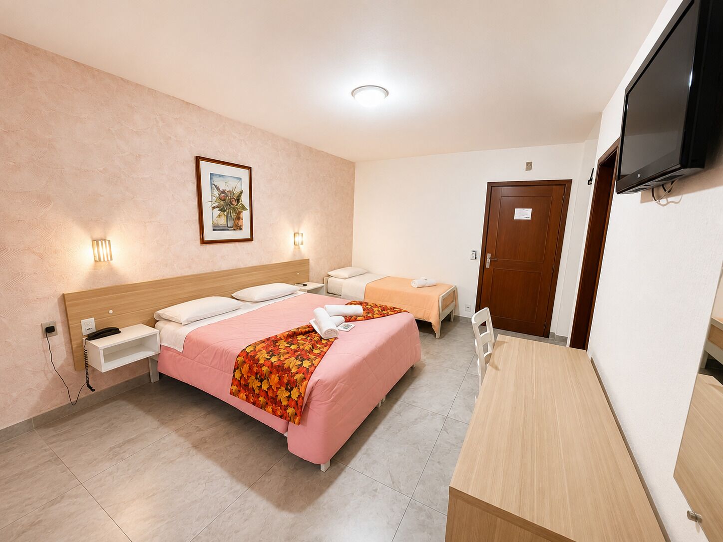 A hotel room with a bed, bedside tables, a desk, a chair, a TV, and a door.