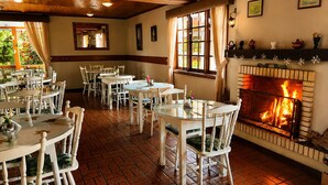 A restaurant with round tables and chairs, a fireplace, and a view of greenery outside. - Hotel Alpenhof (Gramado)