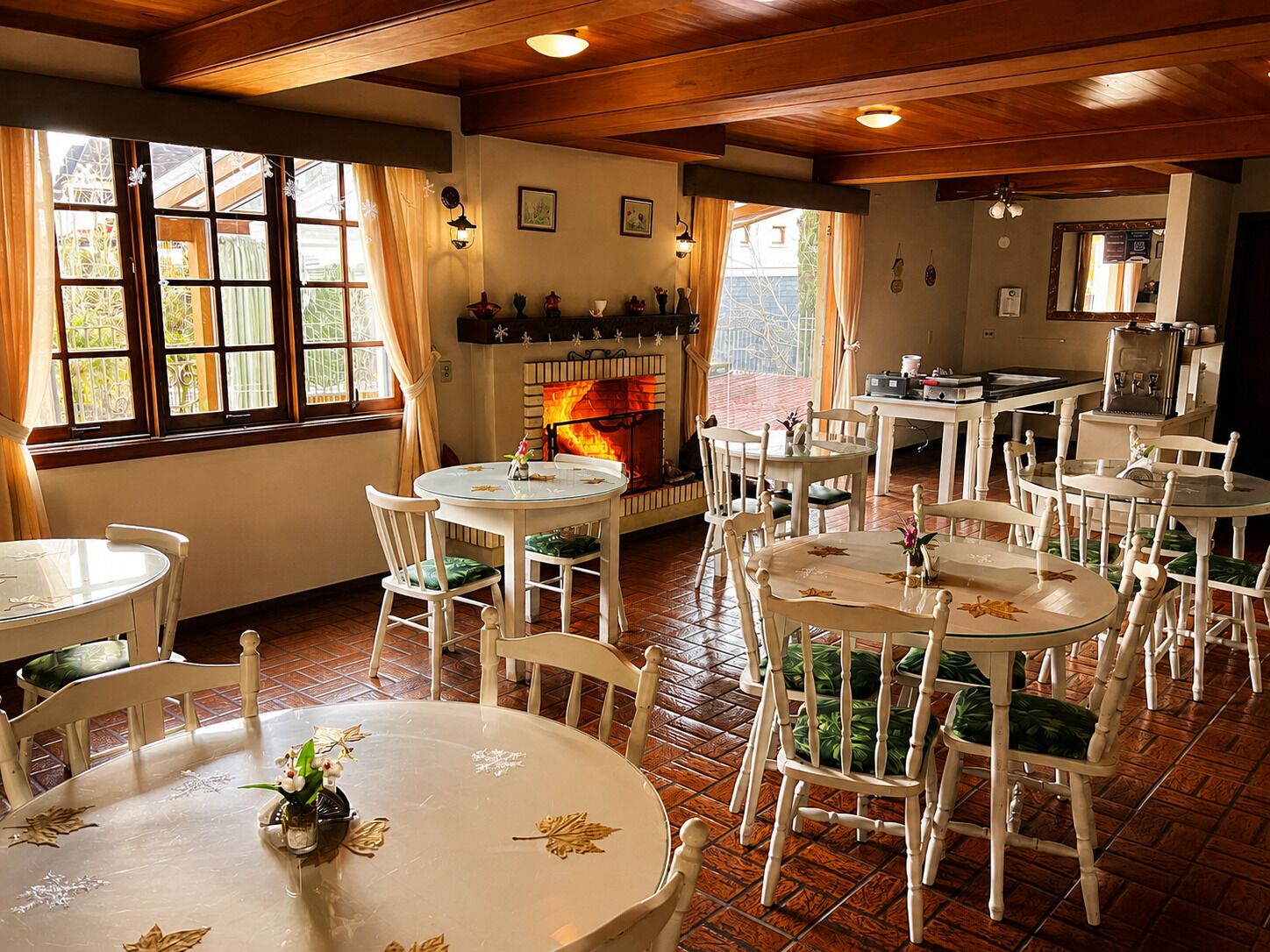 A dining area with round tables and white chairs, a fireplace, and large windows with curtains.