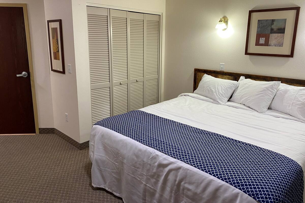 A hotel room with a bed, a wardrobe, a framed picture, and a wall-mounted light fixture.