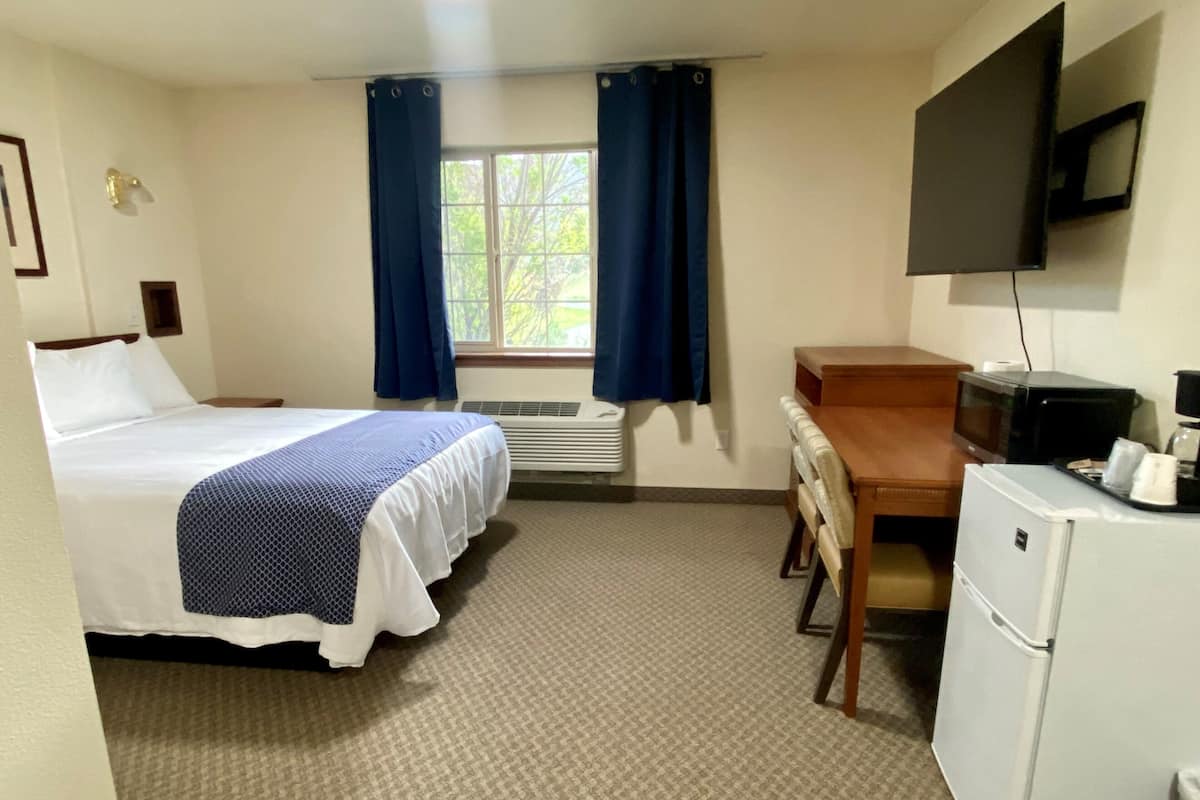 A hotel room with a bed, a desk, a refrigerator, a television, and a window with curtains.