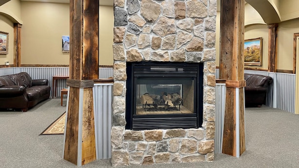 A stone fireplace with a black screen, flanked by wooden columns, in a room with leather sofas and framed pictures on the walls.