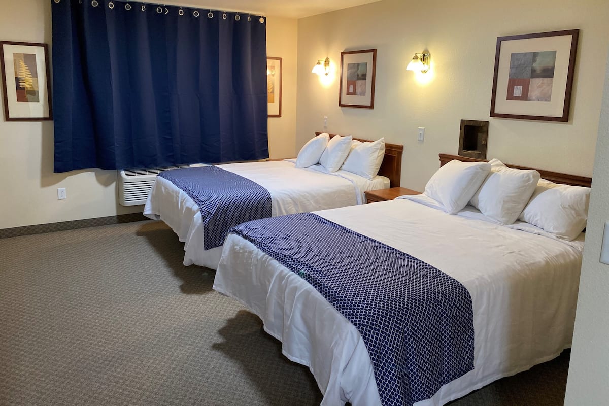A hotel room with two beds, a large window with a blue curtain, wall-mounted lights, and framed artwork.