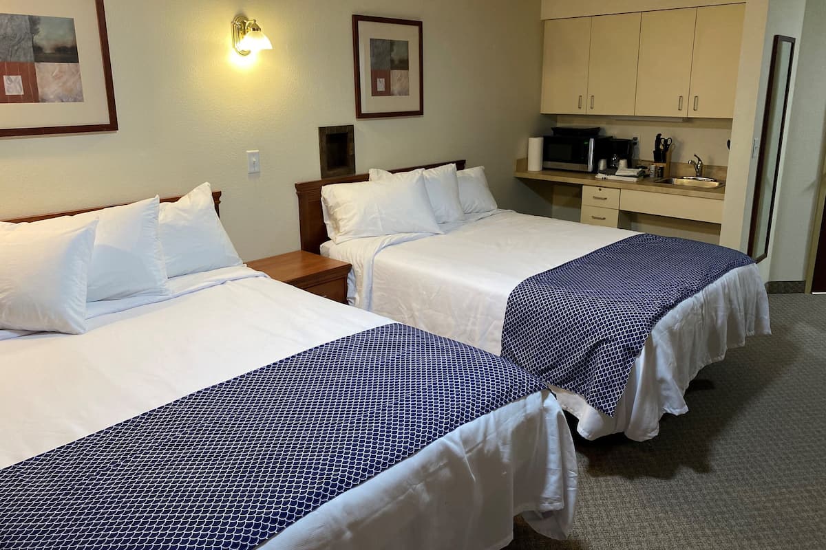 A hotel room with two beds, a small desk with a microwave, and a sink.