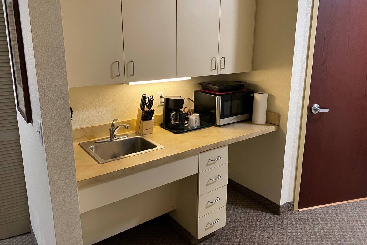 A compact kitchenette with a sink, microwave, coffee maker, and a set of drawers.