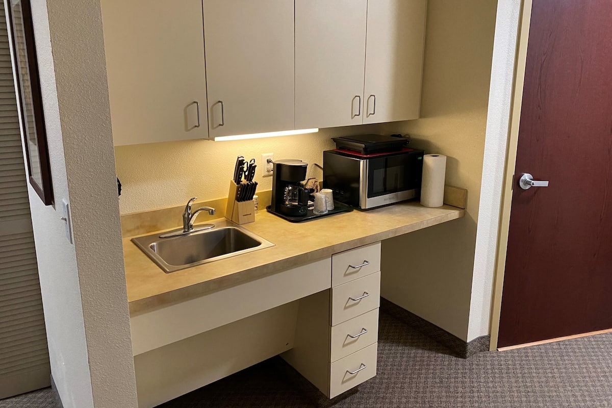 A compact kitchenette with a sink, microwave, coffee maker, and a set of drawers.